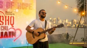 Self-taught musician Ishaq performing live on stage with a guitar during a musical evening event at sunset